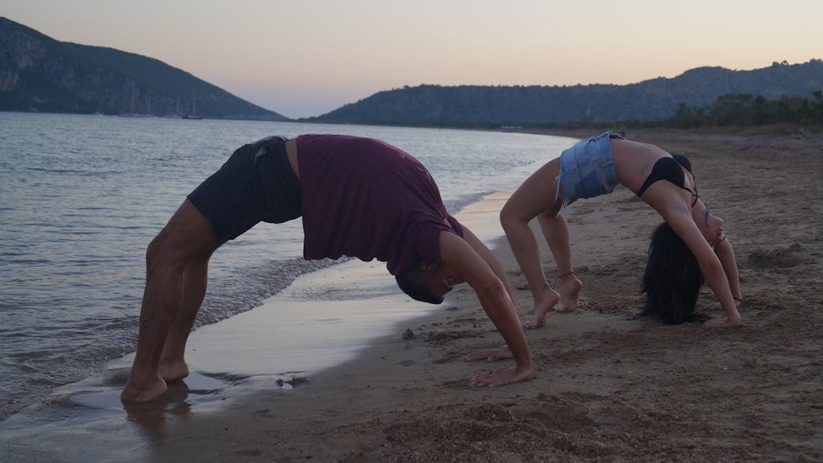 A couple performing yoga poses on Methoni Beach at sunset, showcasing fitness and tranquility.